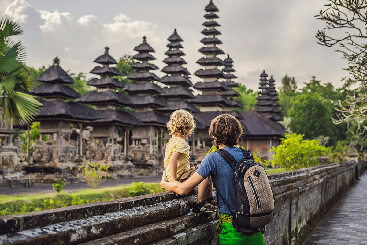 Father & child sitting on a stone wall looking at a temple